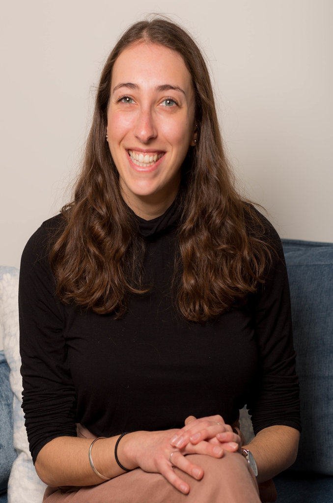 Kaitlyn is looking at the camera and smiling. She is wearing a black shirt and her hands are crossed on her lap.