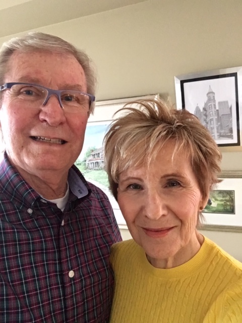 Ron (left) is smiling into camera. he is wearing glasses and a checkered shirt. Catherine (right) is smiling into camera and wearing a yellow shirt.